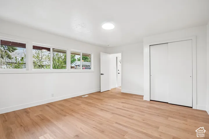 Spacious room featuring wood-finish flooring, white walls, and bright overhead lighting