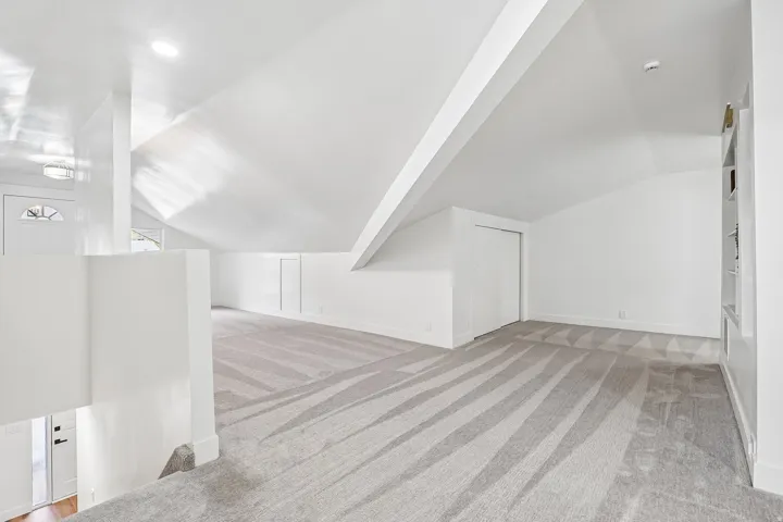 Spacious carpeted room featuring an angled ceiling, recessed lighting, built-in shelving, and a white sliding closet door