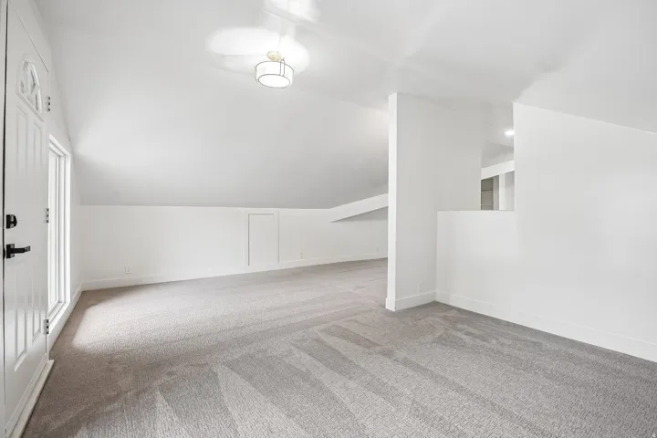 Expansive carpeted area featuring a white door with a window, white walls, and a contemporary flush mount light fixture