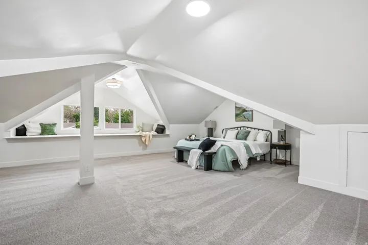 Spacious attic room with light gray carpeting and sloped white ceilings