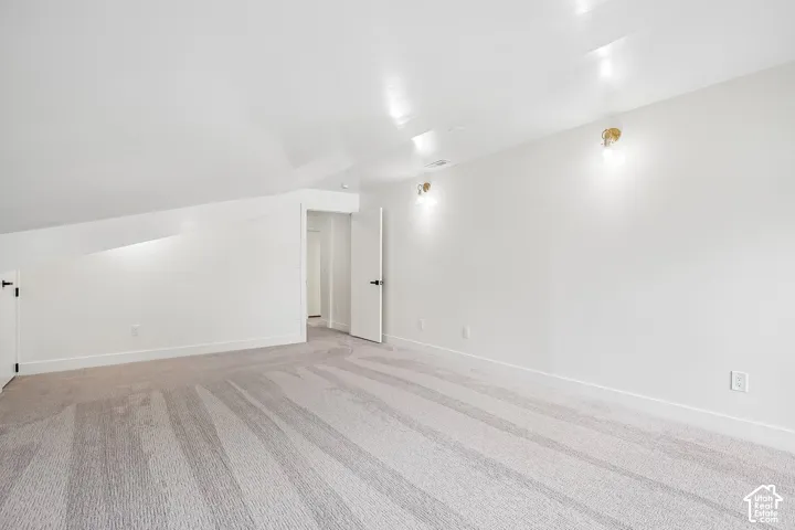 Spacious room with sloped ceilings, light-toned carpet, white walls, recessed ceiling lights, and two wall sconces
