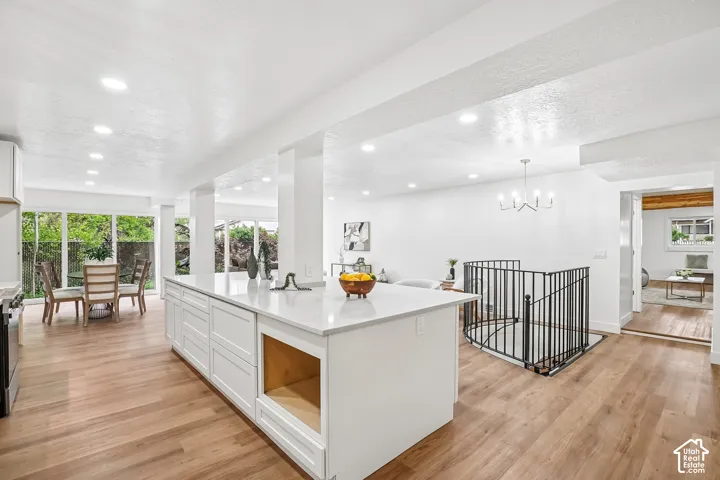 Expansive kitchen island with a light-toned countertop, wood-finish flooring, recessed lighting, white cabinetry, and a black metal spindle staircase