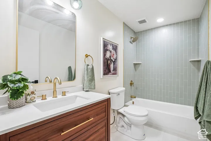 Bathroom featuring a wood-finish vanity with a white countertop and rectangular undermount sink, brushed gold hardware and faucet, and a shower-tub combination with light green subway tile surround and integrated shelving