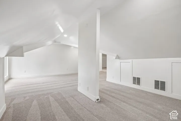 Spacious attic space featuring sloped ceilings, recessed lighting, neutral-toned carpet, built-in access panels, and baseboard trim