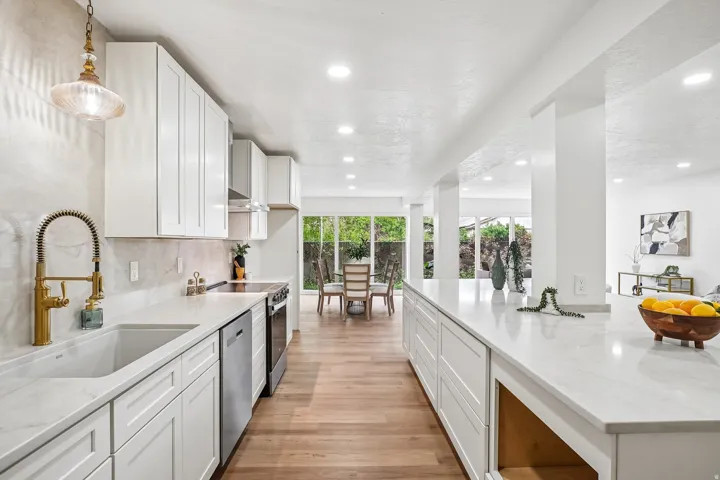 Contemporary kitchen featuring white cabinetry, light-toned countertops, a gold-finish faucet, recessed lighting, and wood-finish flooring