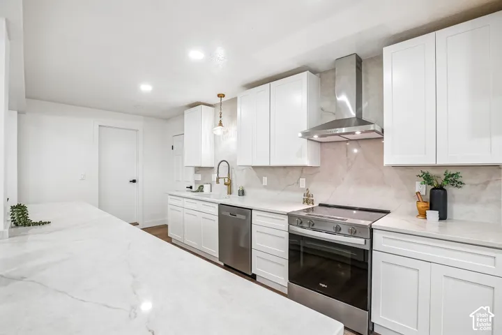 Kitchen featuring white shaker cabinetry, light-toned countertops with subtle veining, a stainless steel range with matching hood vent, a stainless steel dishwasher, and a gold-toned gooseneck faucet