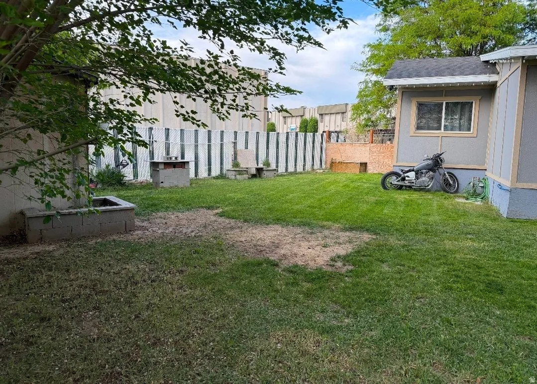 Expansive backyard featuring a partial chain-link fence, a concrete block planter, and a built-in outdoor grill