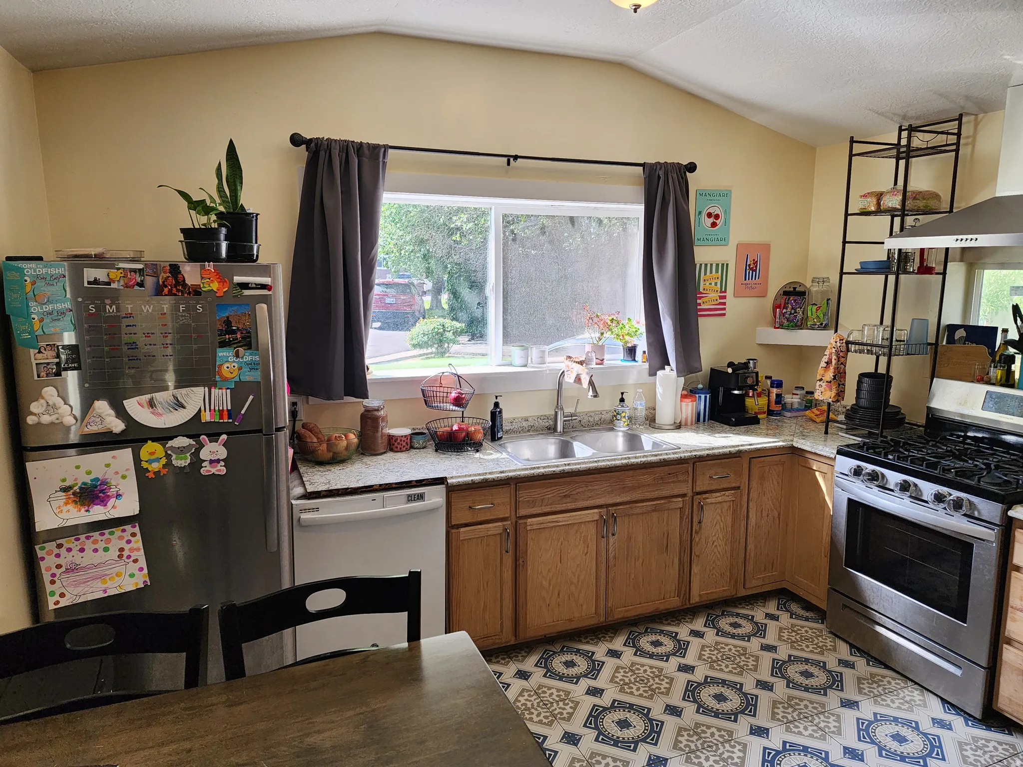 Kitchen featuring vaulted ceilings, wood cabinetry, patterned floor tiling, stainless steel double basin sink, and a stainless steel gas range with overhead ventilation