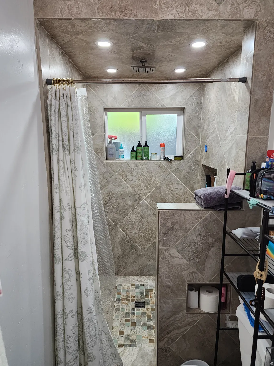 Tiled shower enclosure featuring a square rainfall showerhead, recessed lighting, and a built-in window
