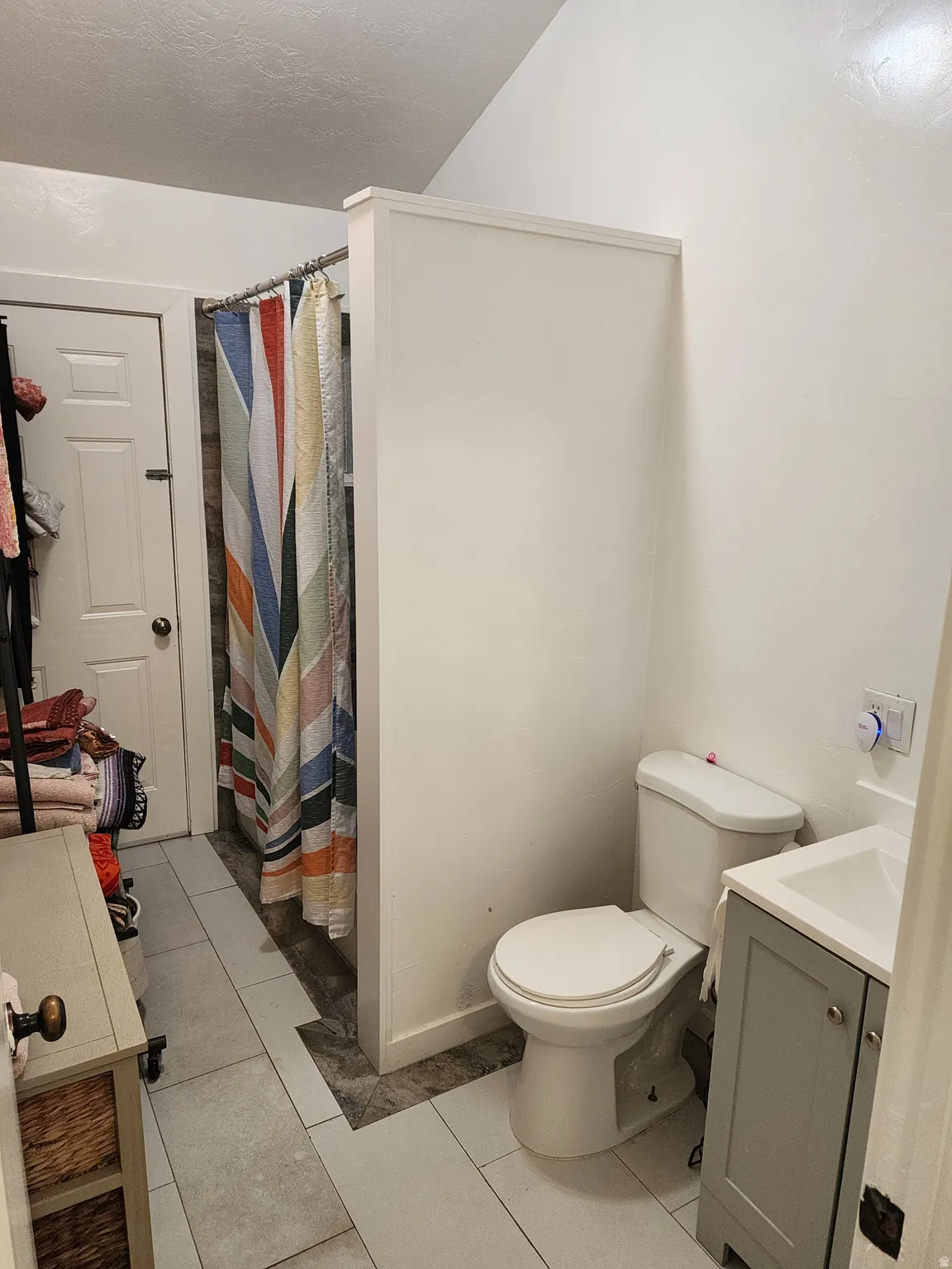 Bathroom featuring a white toilet, a gray vanity with a white sink, and light-colored tile flooring