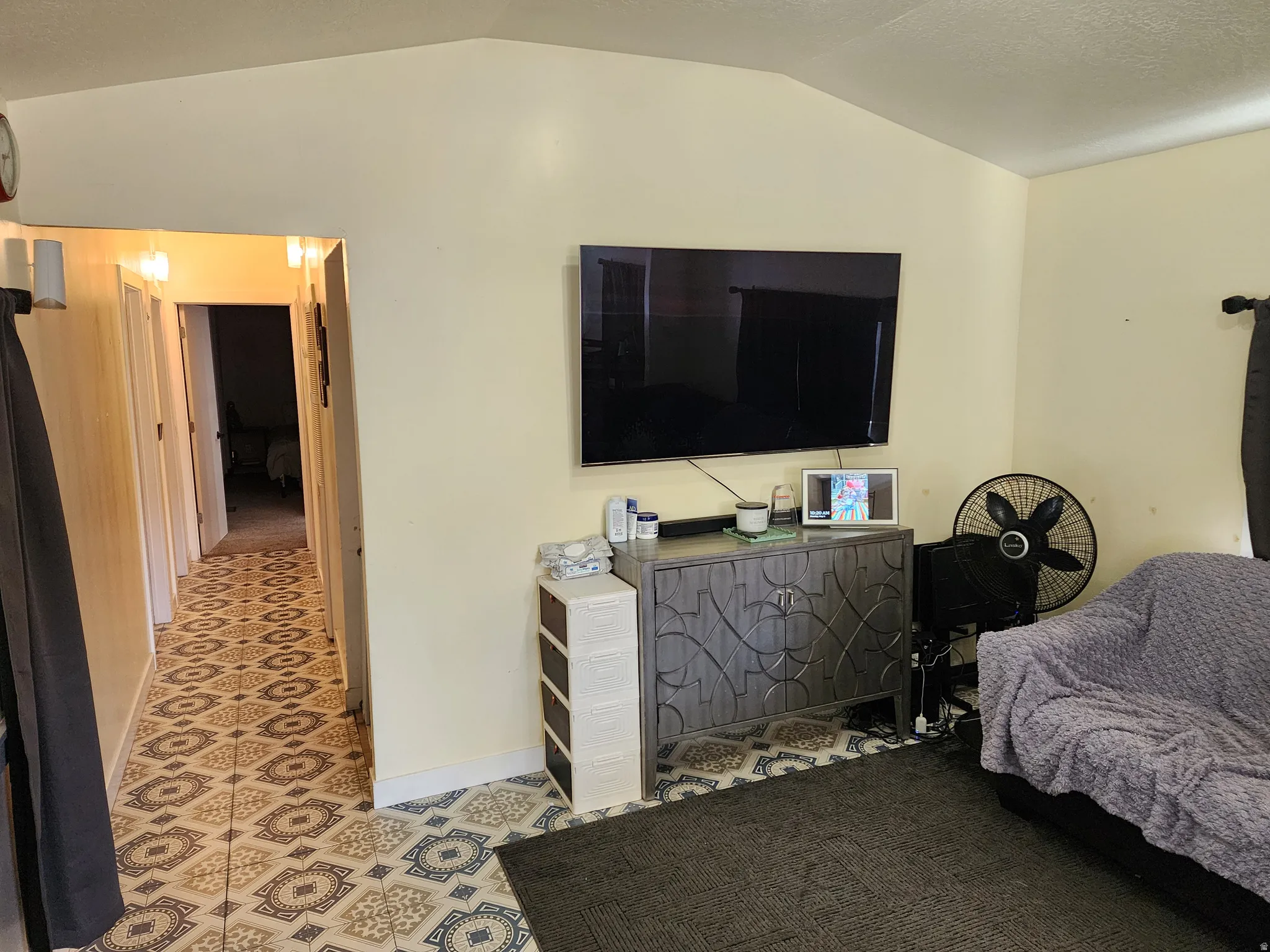Vaulted ceiling living area featuring a decorative console cabinet, wall-mounted television, and patterned flooring extending into the hallway