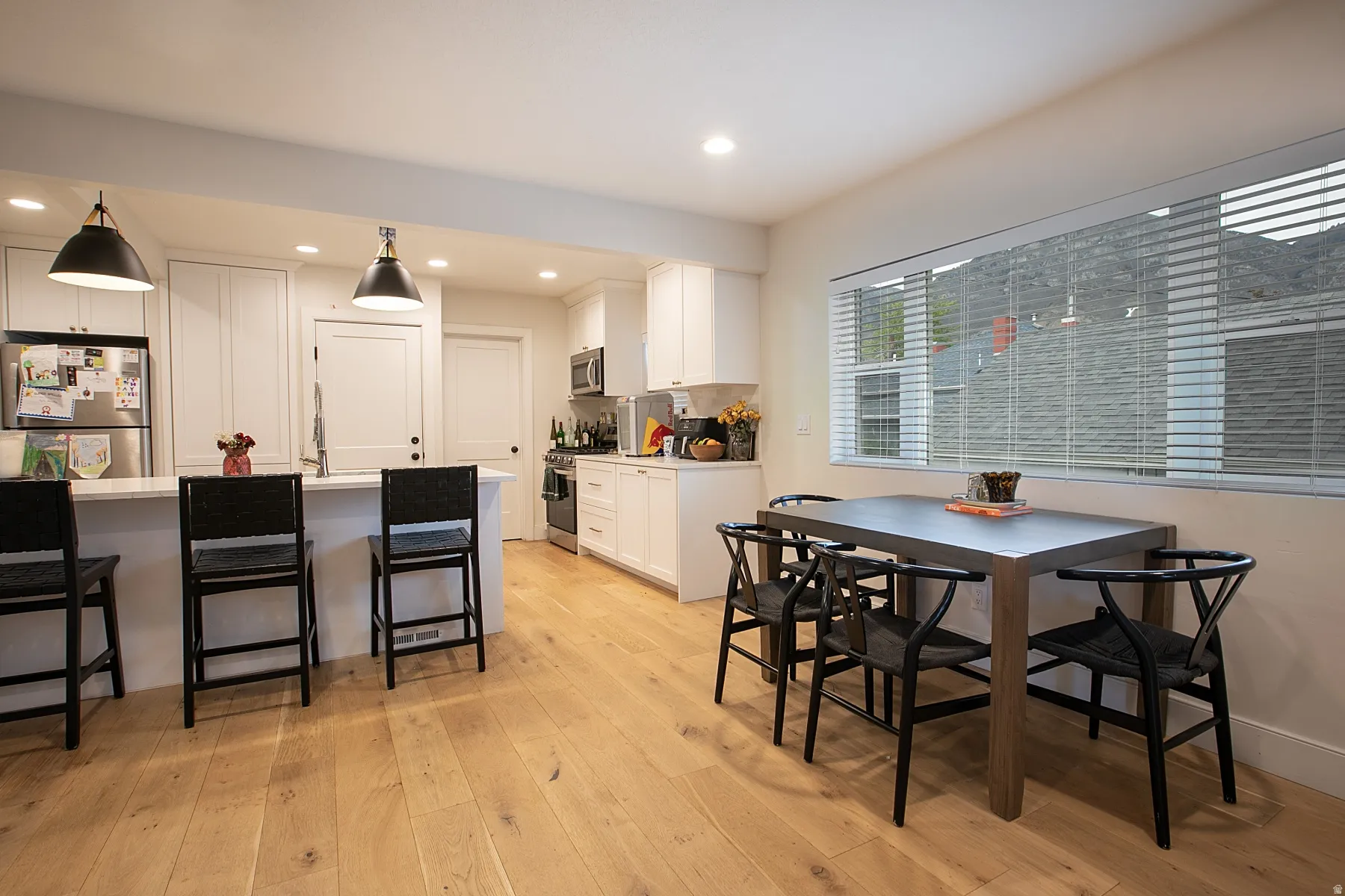 Kitchen with stainless steel appliances, a kitchen bar, white cabinets, light wood-type flooring, and hanging light fixtures