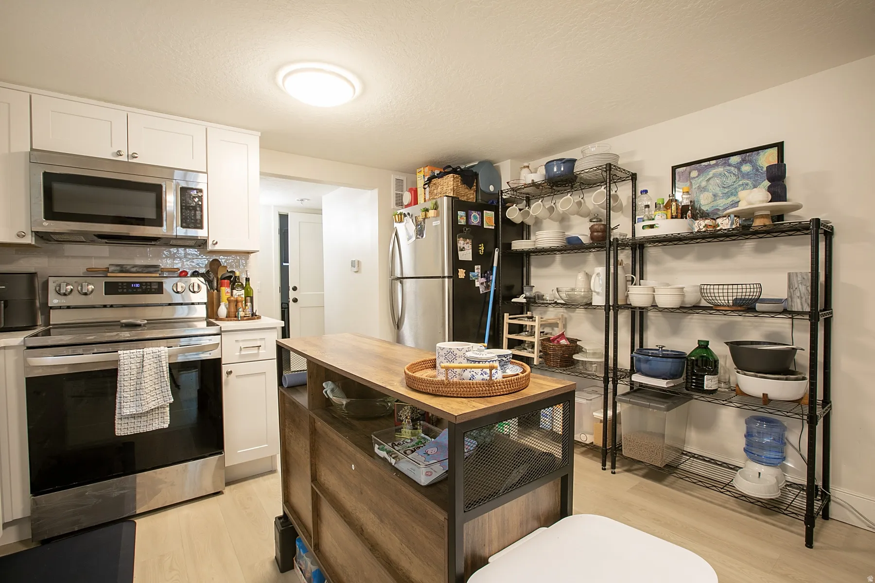 Kitchen with stainless steel appliances, white cabinetry, light wood-type flooring, backsplash, and butcher block counters