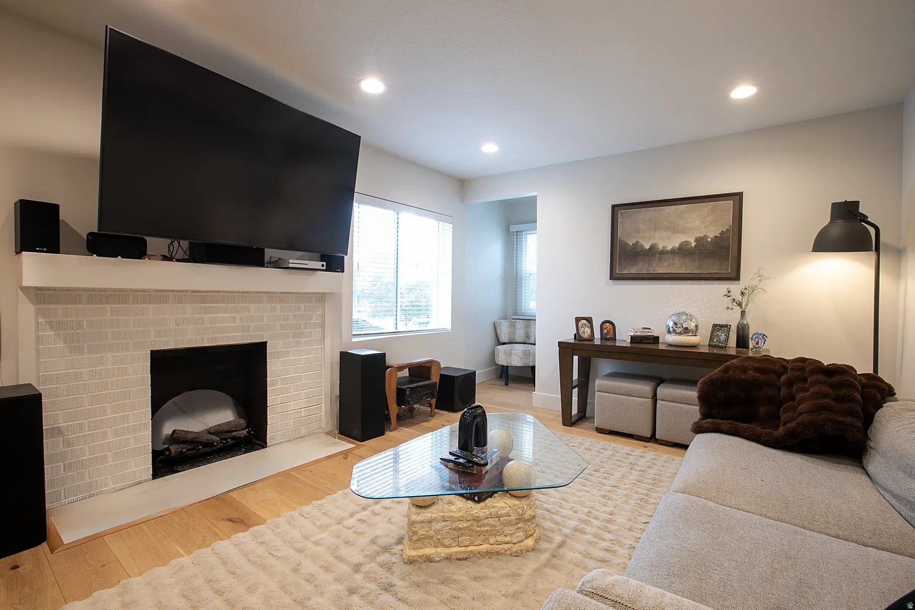 Living room with light wood finished floors, a brick fireplace, and recessed lighting