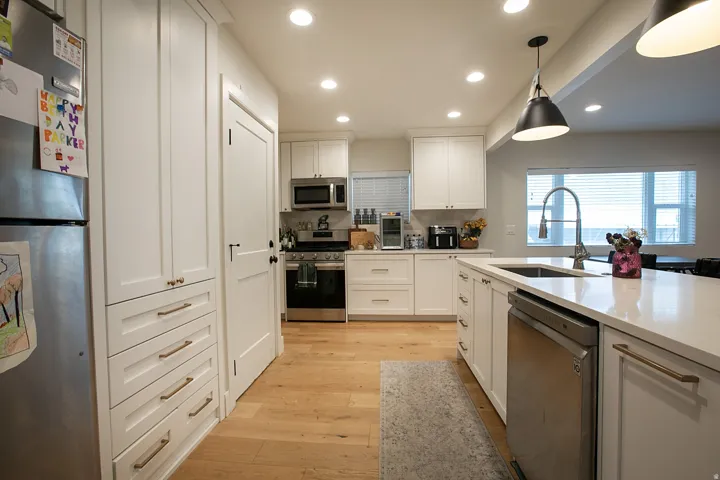 Kitchen with stainless steel appliances, white cabinets, light wood-type flooring, decorative light fixtures, and light stone countertops