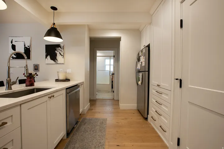 Kitchen with white cabinets, stainless steel appliances, light wood-type flooring, light stone counters, and hanging light fixtures