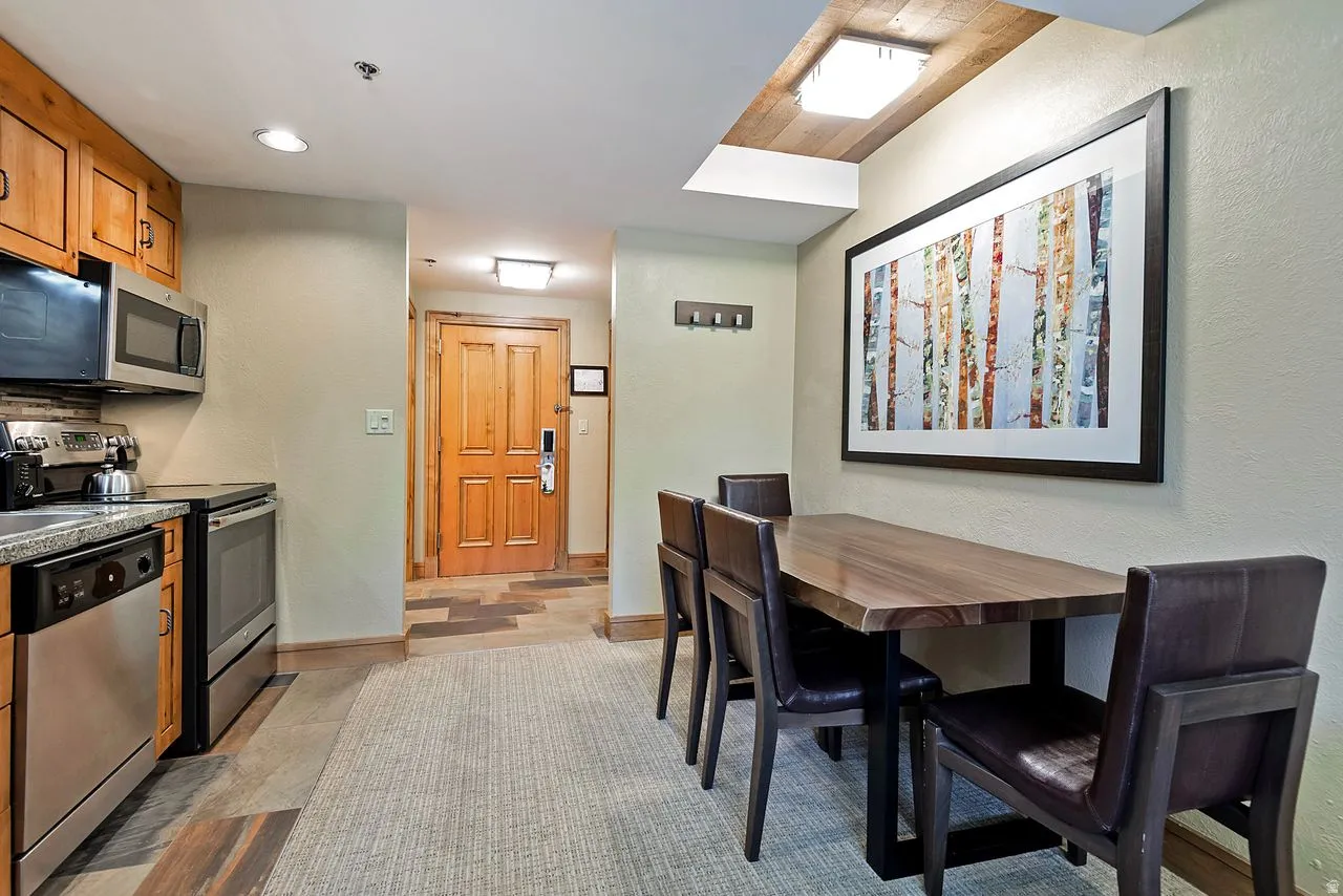 Open-concept kitchen and dining area featuring stainless steel appliances, wood-finish cabinetry, recessed lighting, a built-in microwave, and a granite-style countertop