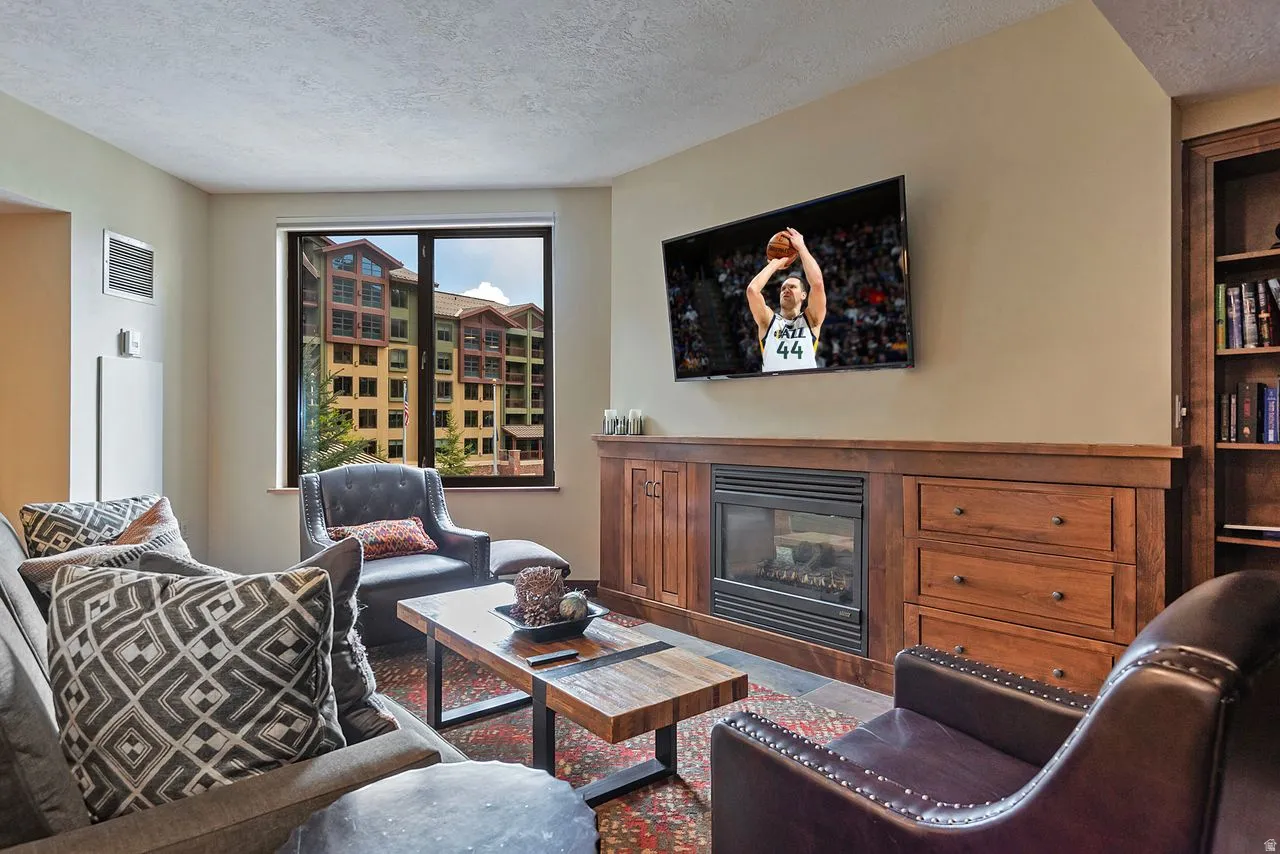 Living area featuring a built-in wood media console with integrated fireplace, wood-finish flooring, and a large window