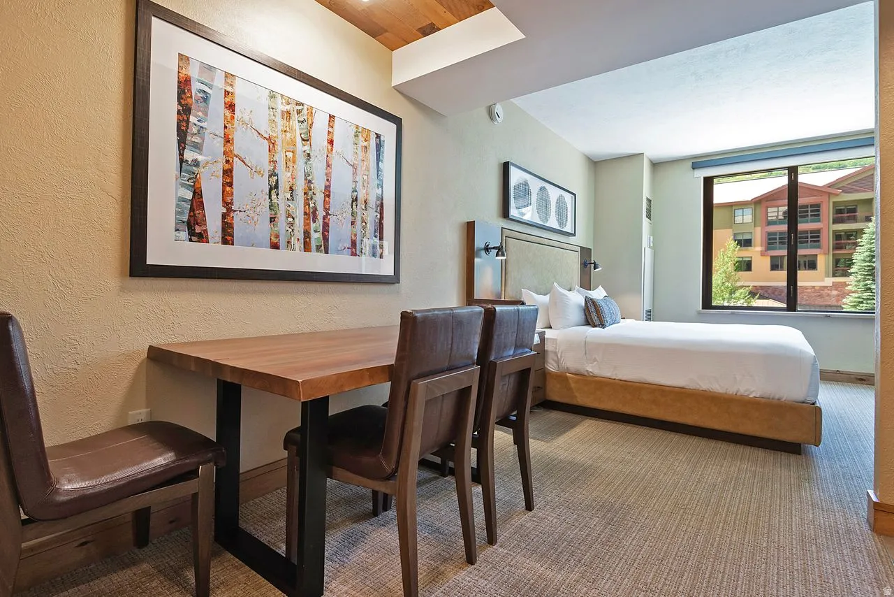 Open concept room featuring a wood-finish dining table with metal base, a built-in upholstered headboard, and integrated wall sconces