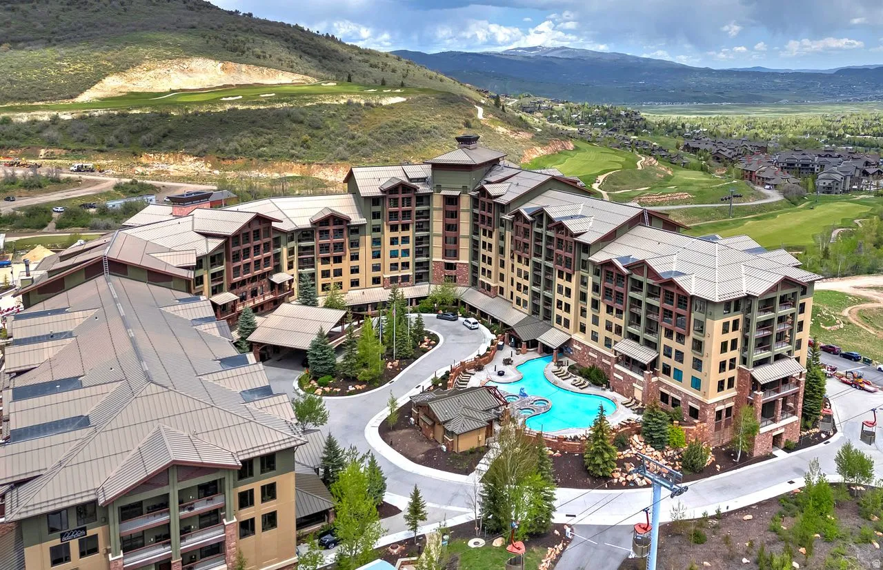 Expansive resort-style property featuring a large outdoor swimming pool with integrated spa, multiple building structures with varied rooflines, a porte-cochère entrance, and surrounding mountainous terrain with golf course elements