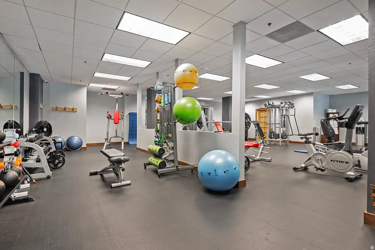 Dedicated fitness area featuring durable rubber flooring, mirrored wall, recessed lighting, and support columns