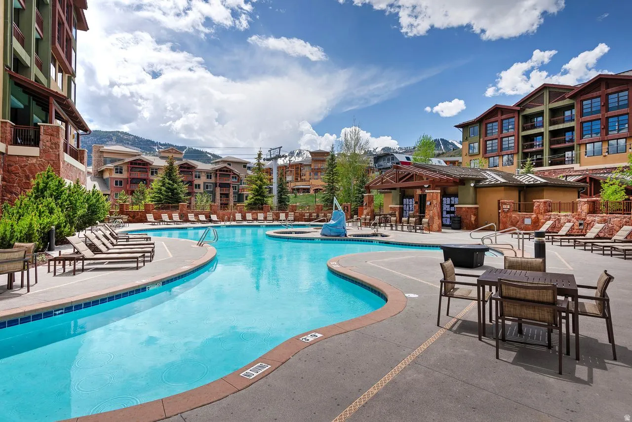 Resort-style outdoor pool area featuring a freeform swimming pool, integrated spa, ample lounge seating, and a mountainside backdrop