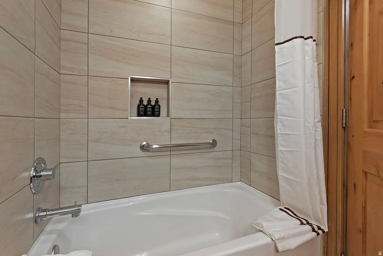 Bathtub-shower combination featuring light-toned tile surround, polished chrome fixtures, an integrated shower niche, and a chrome grab bar