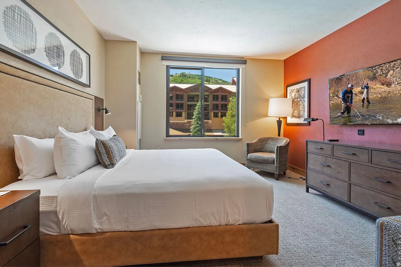 Spacious bedroom featuring a large window, neutral carpeting, a built-in upholstered headboard, and a multi-drawer dresser
