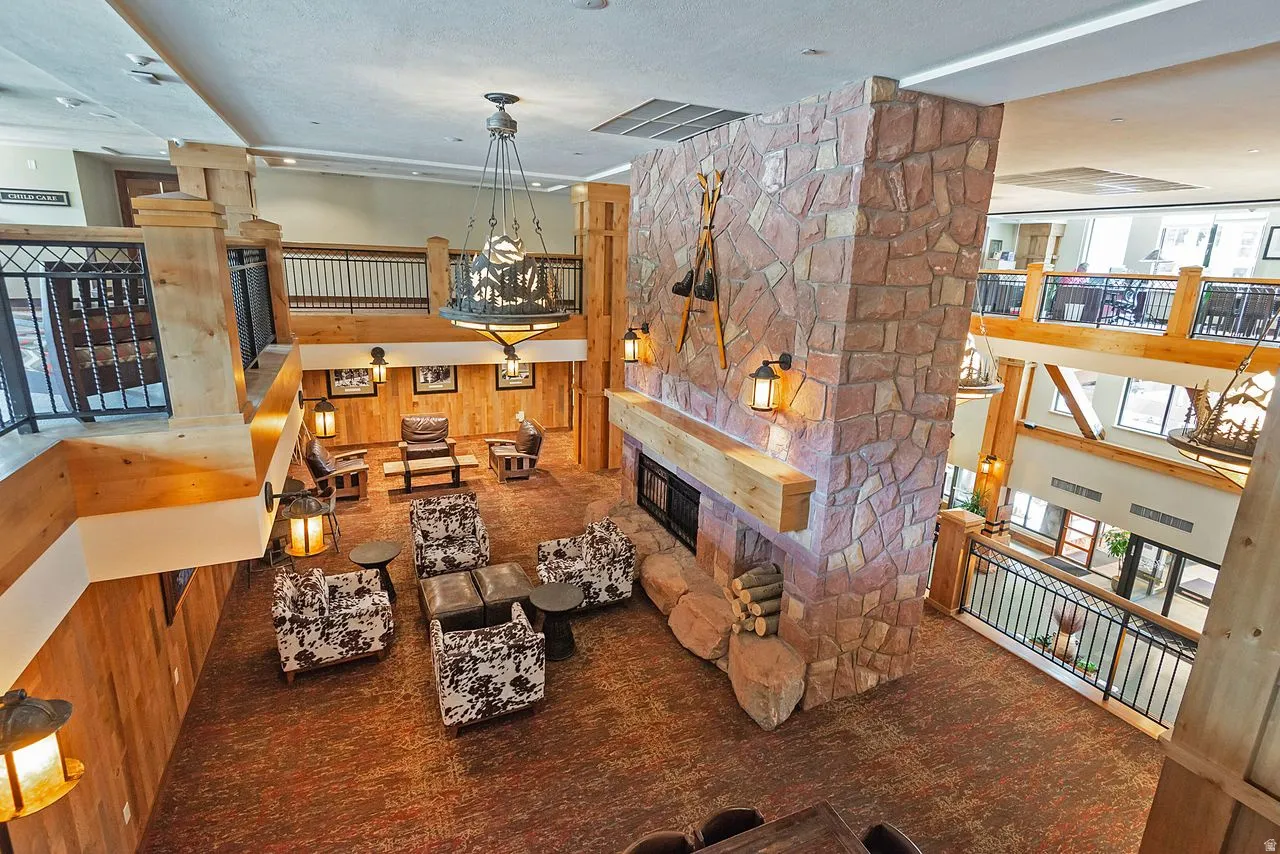 Two-story great room with a stone fireplace, wood-finish wall paneling, wrought iron railings, and exposed wood beams