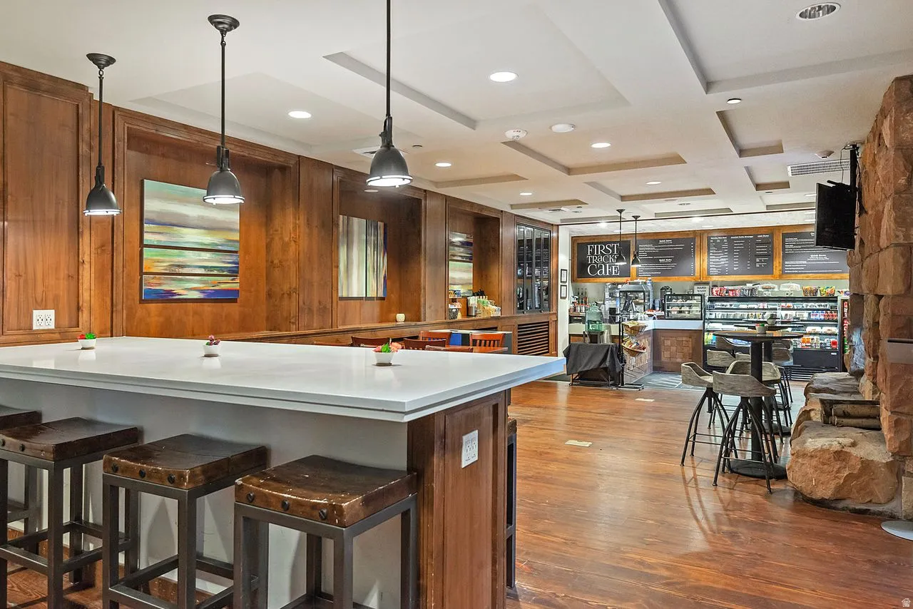 Spacious community room featuring extensive wood paneling, wood-finish flooring, a stone accent wall, and a coffered ceiling