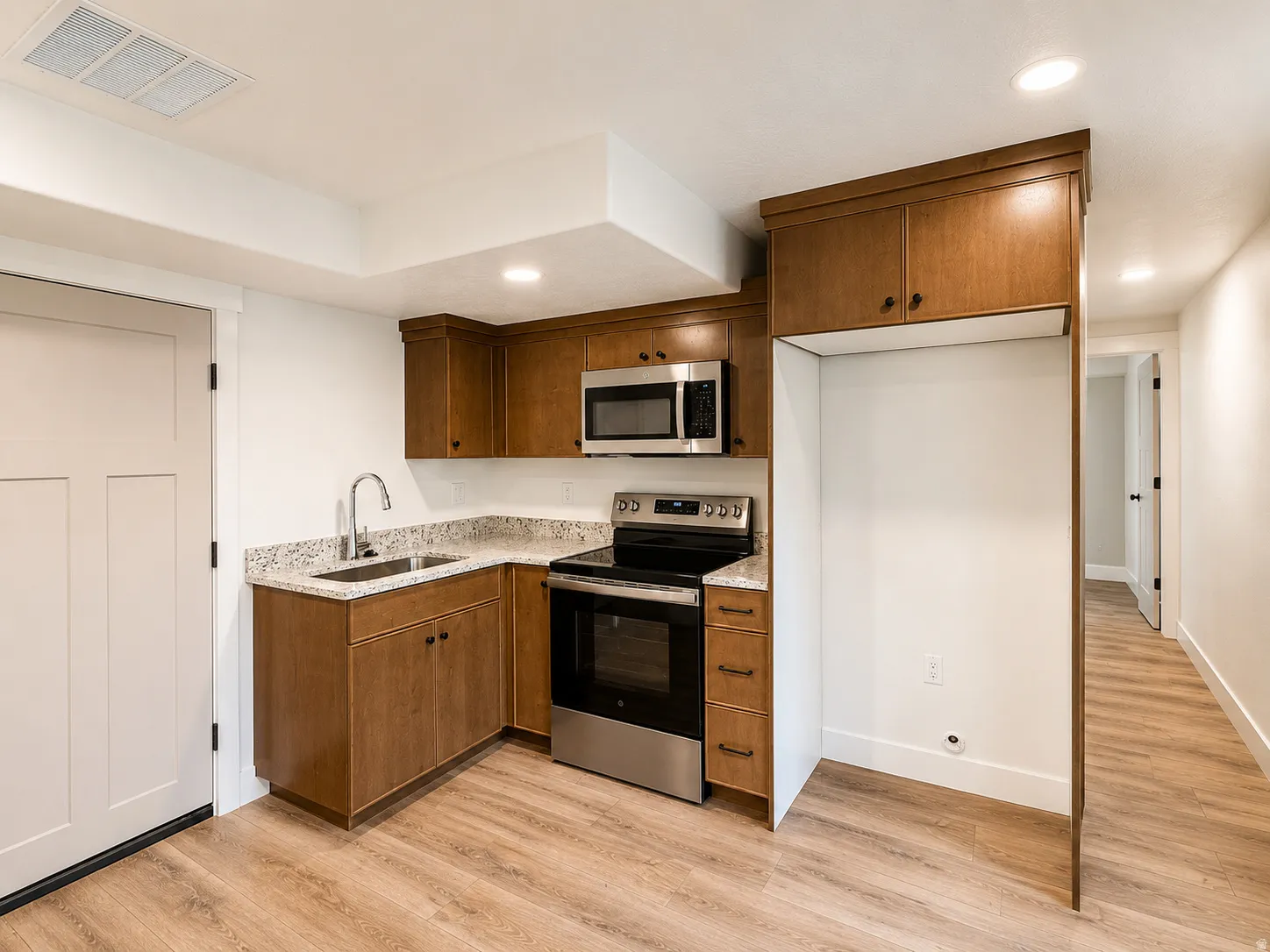 Kitchenette featuring wood-finish cabinetry, stainless steel appliances, and light granite countertops