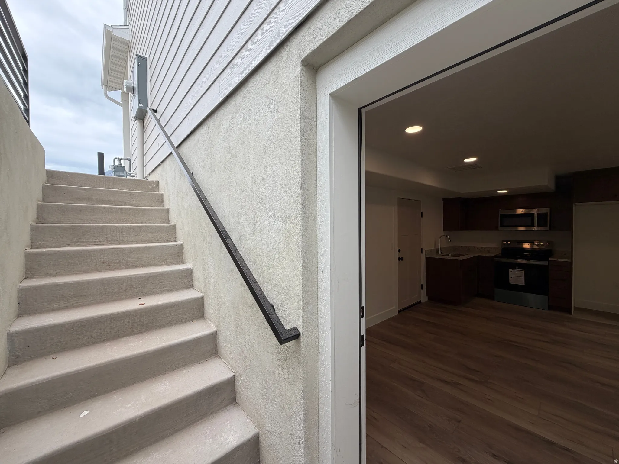 Exterior concrete staircase with a black metal handrail leading to a ground-level entrance
