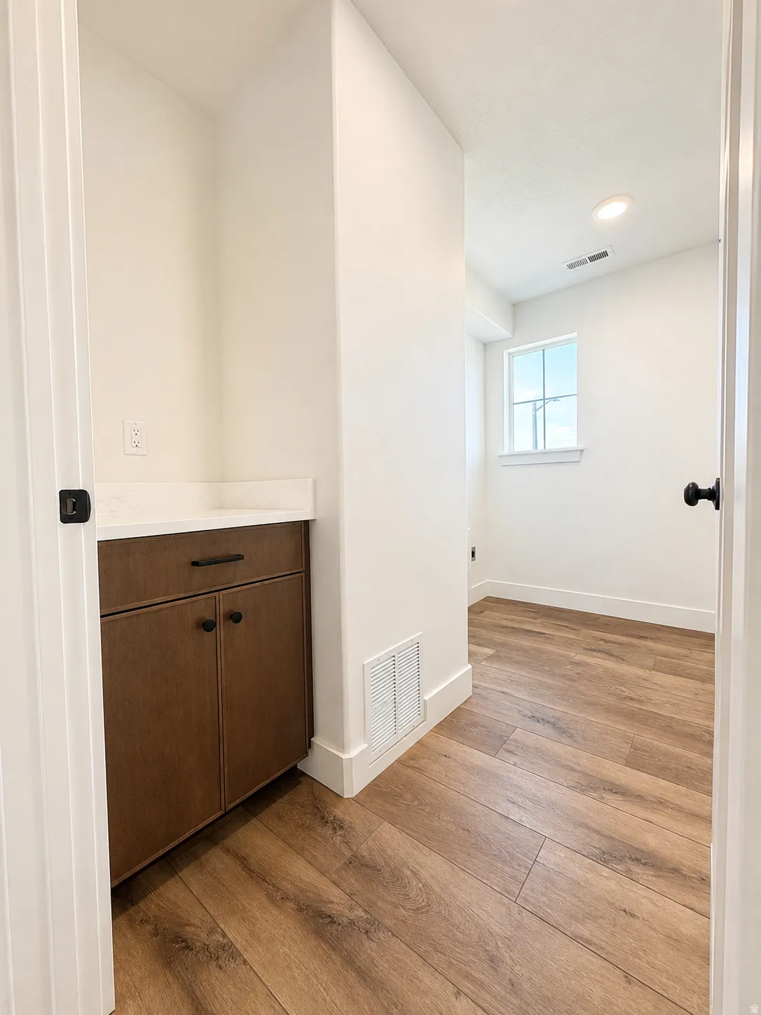 Built-in vanity with wood-finish cabinetry, a light-toned countertop, and matte black hardware