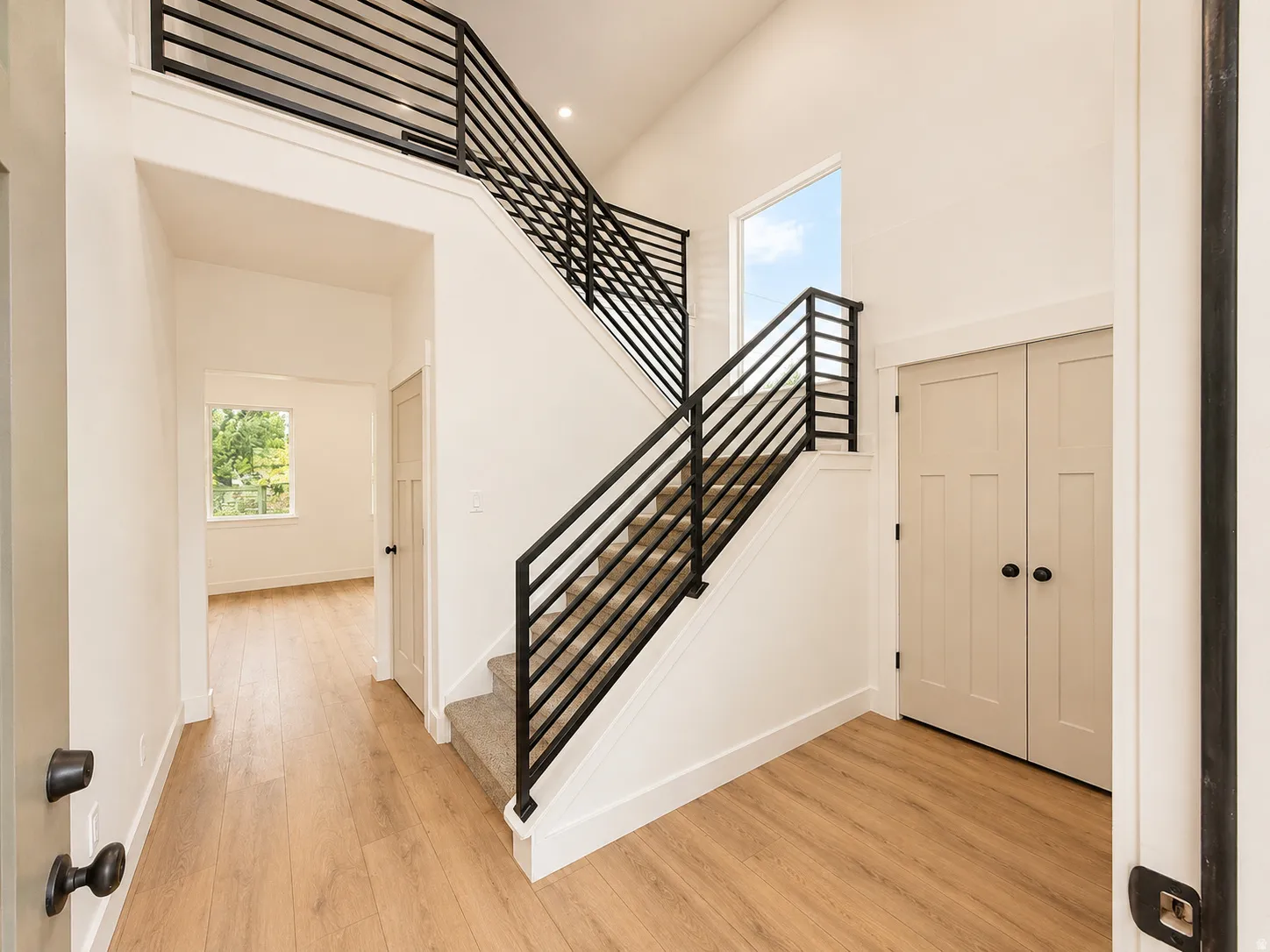 Two-story foyer featuring wood-finish flooring and a modern staircase with black metal railings and carpeted treads