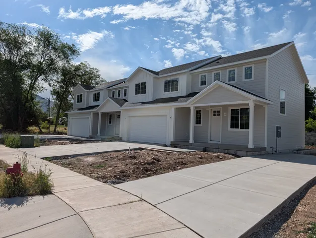 Newly constructed multi-unit property featuring light-colored siding, multiple windows, attached garages, covered entryways, and concrete driveways