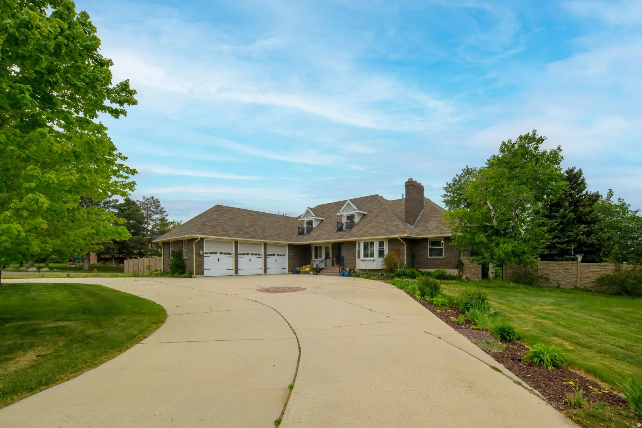 Curved concrete driveway leading to a brick residence with a three-car garage