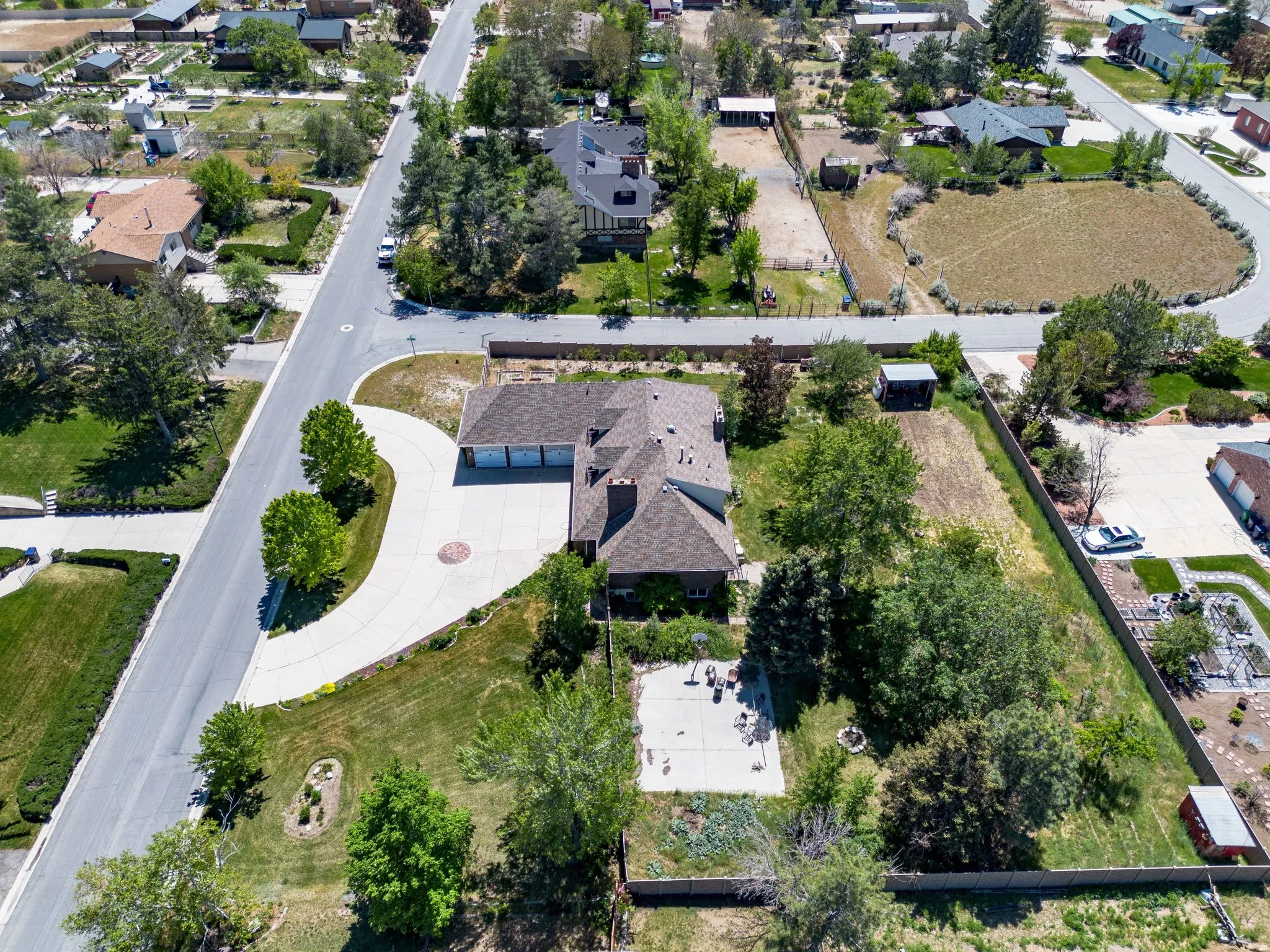Expansive property featuring a curved driveway, three-car garage, established trees, a concrete patio, and a fire pit area