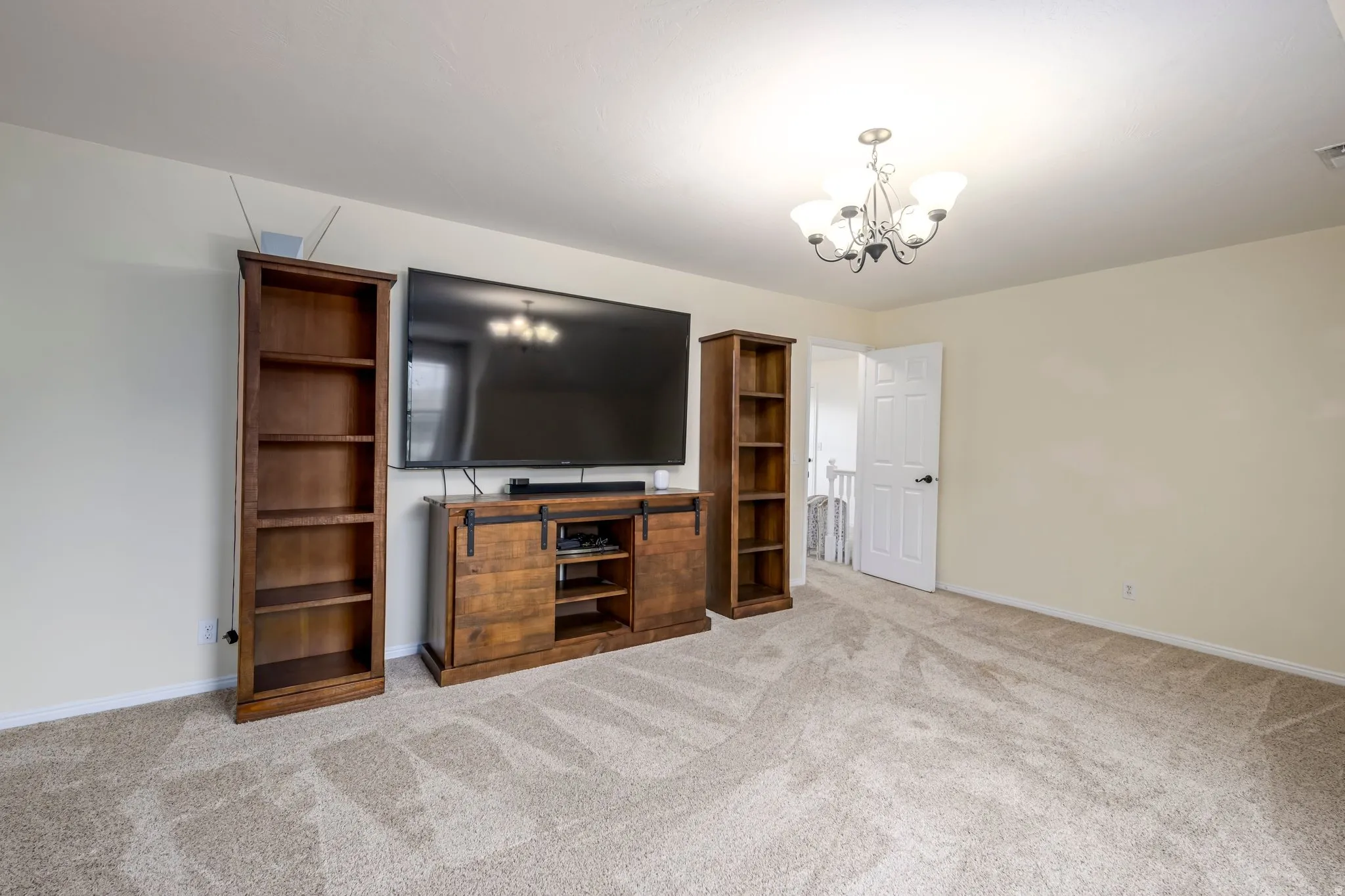 Spacious room featuring neutral carpeting, light-toned walls, and a ceiling-mounted chandelier