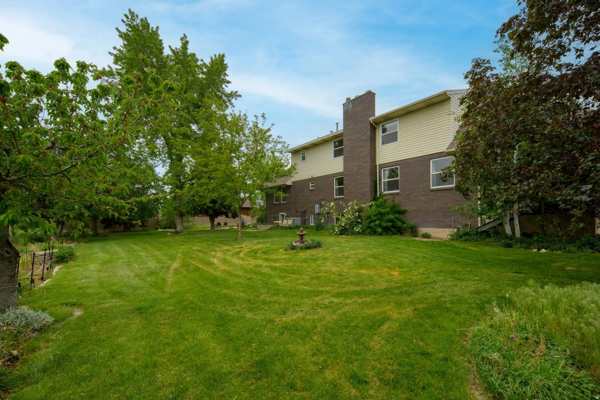 Expansive backyard featuring a manicured lawn, mature trees, and a two-story residence with brick and siding exterior
