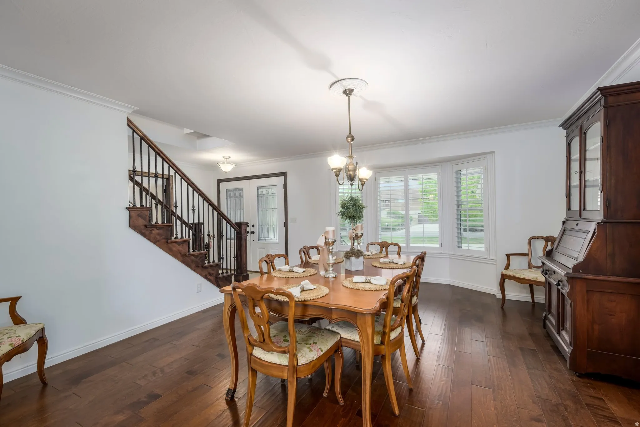Dining area featuring wood-finish flooring, a decorative chandelier, and a bay window with plantation shutters