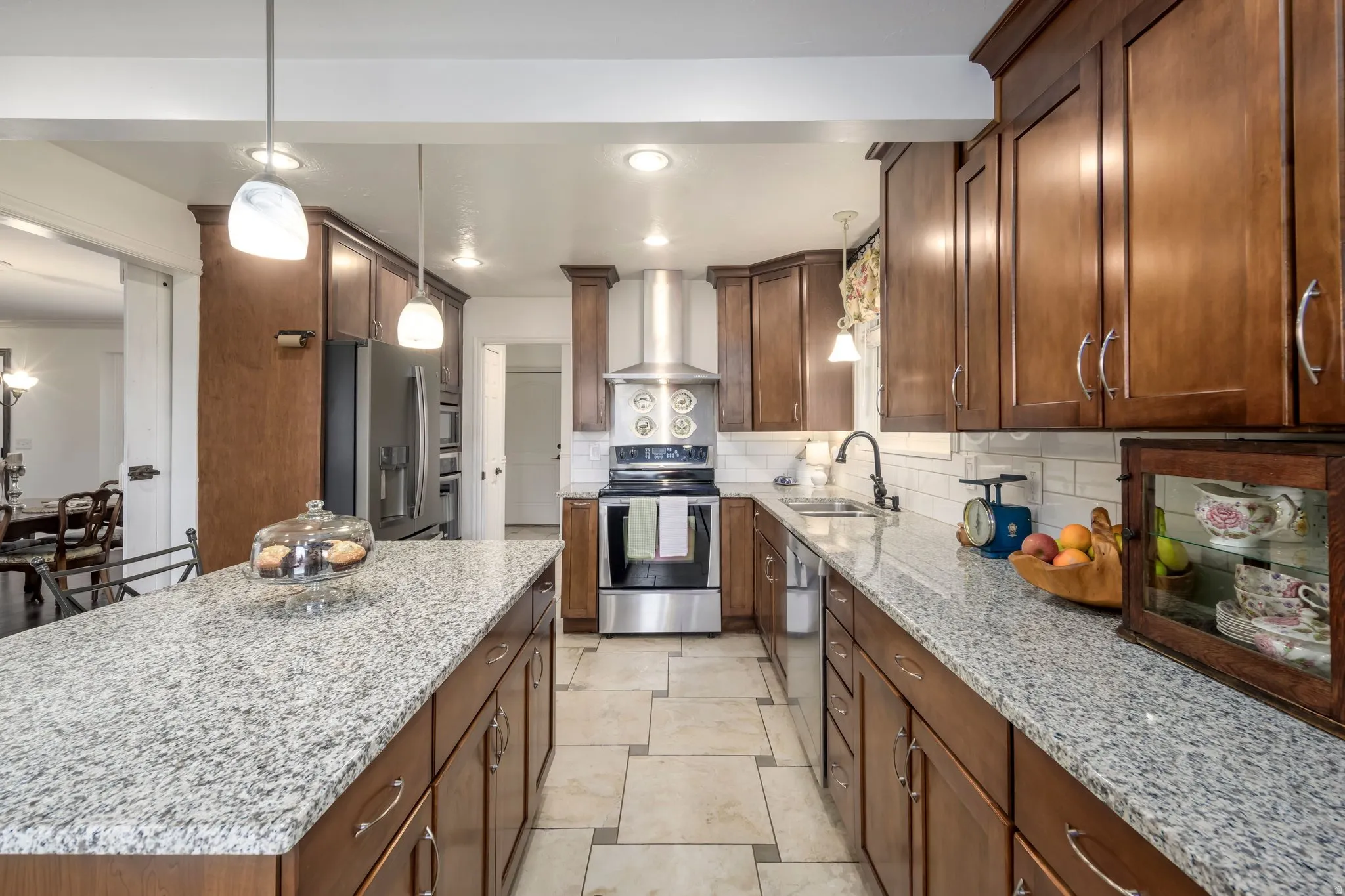 Kitchen featuring wood cabinetry, light-toned countertops, tile flooring, stainless steel appliances, and pendant lighting