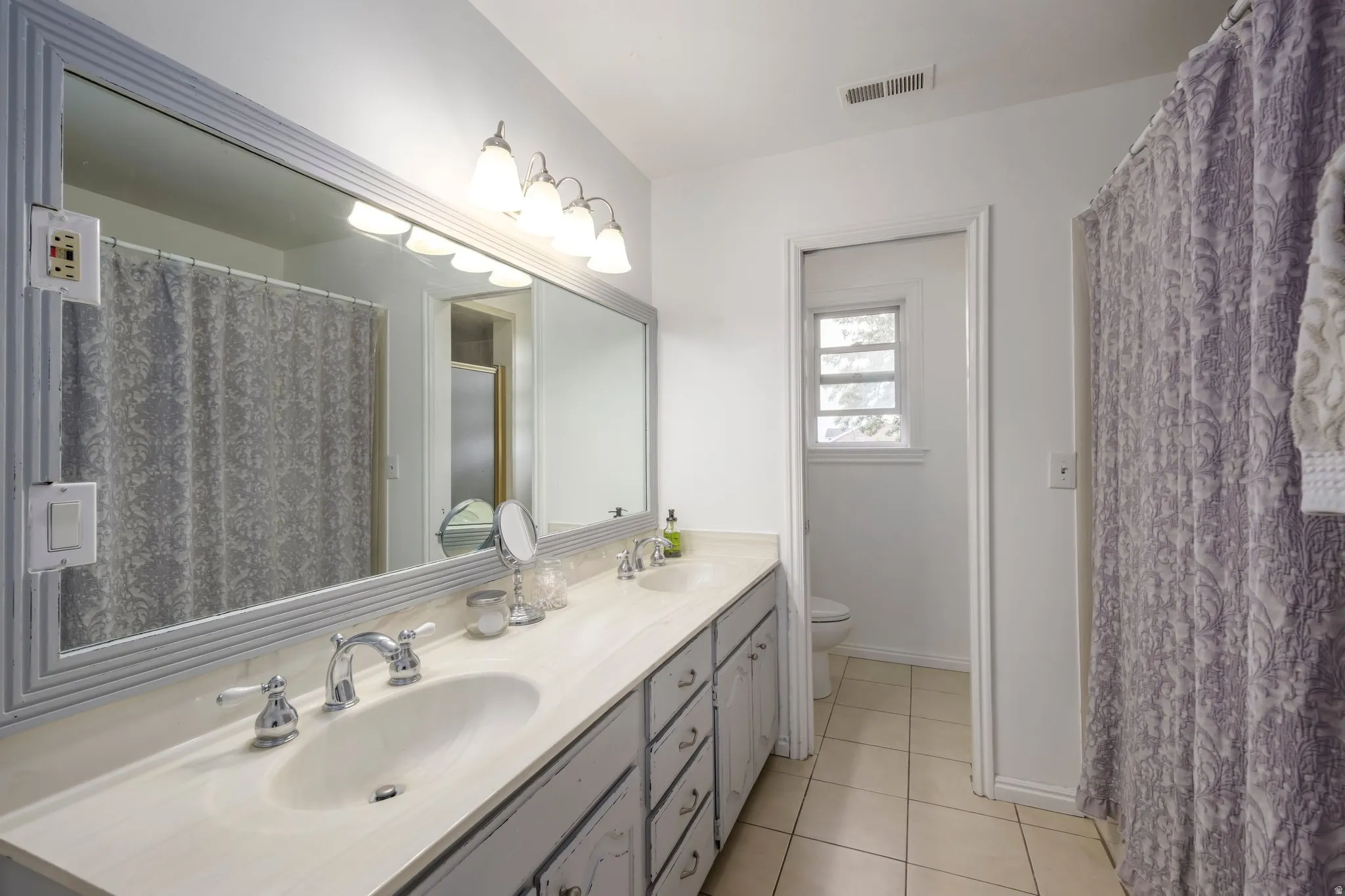 Vanity with dual integrated sinks, chrome hardware, and a large framed mirror with overhead lighting