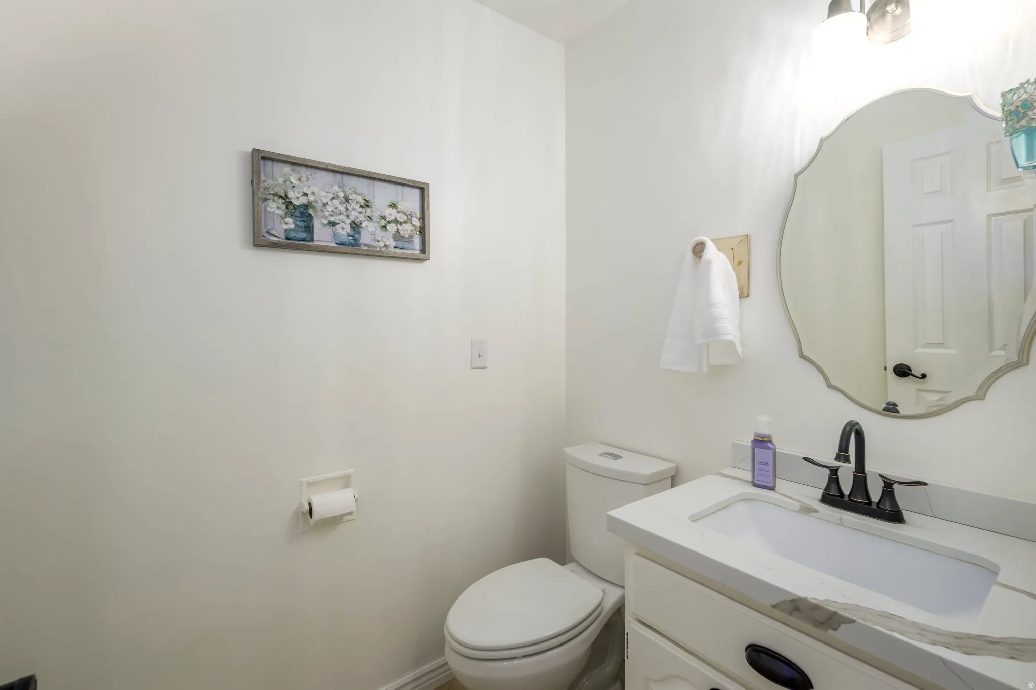 Bathroom featuring a vanity with a white countertop and integrated sink, dark bronze faucet, and a decorative mirror
