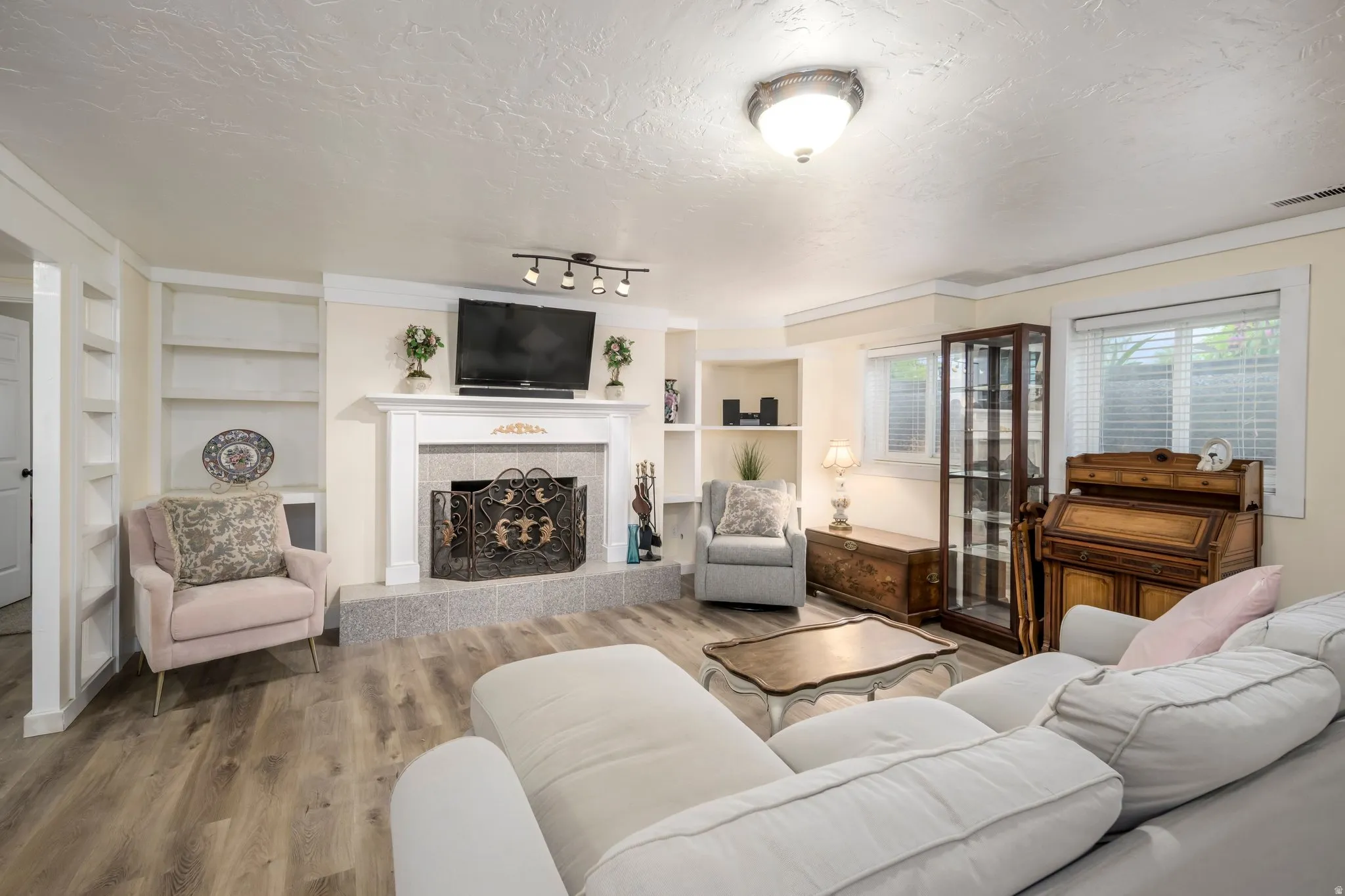 Spacious living area featuring wood-finish flooring, a white mantel fireplace with a decorative metal screen, and built-in shelving