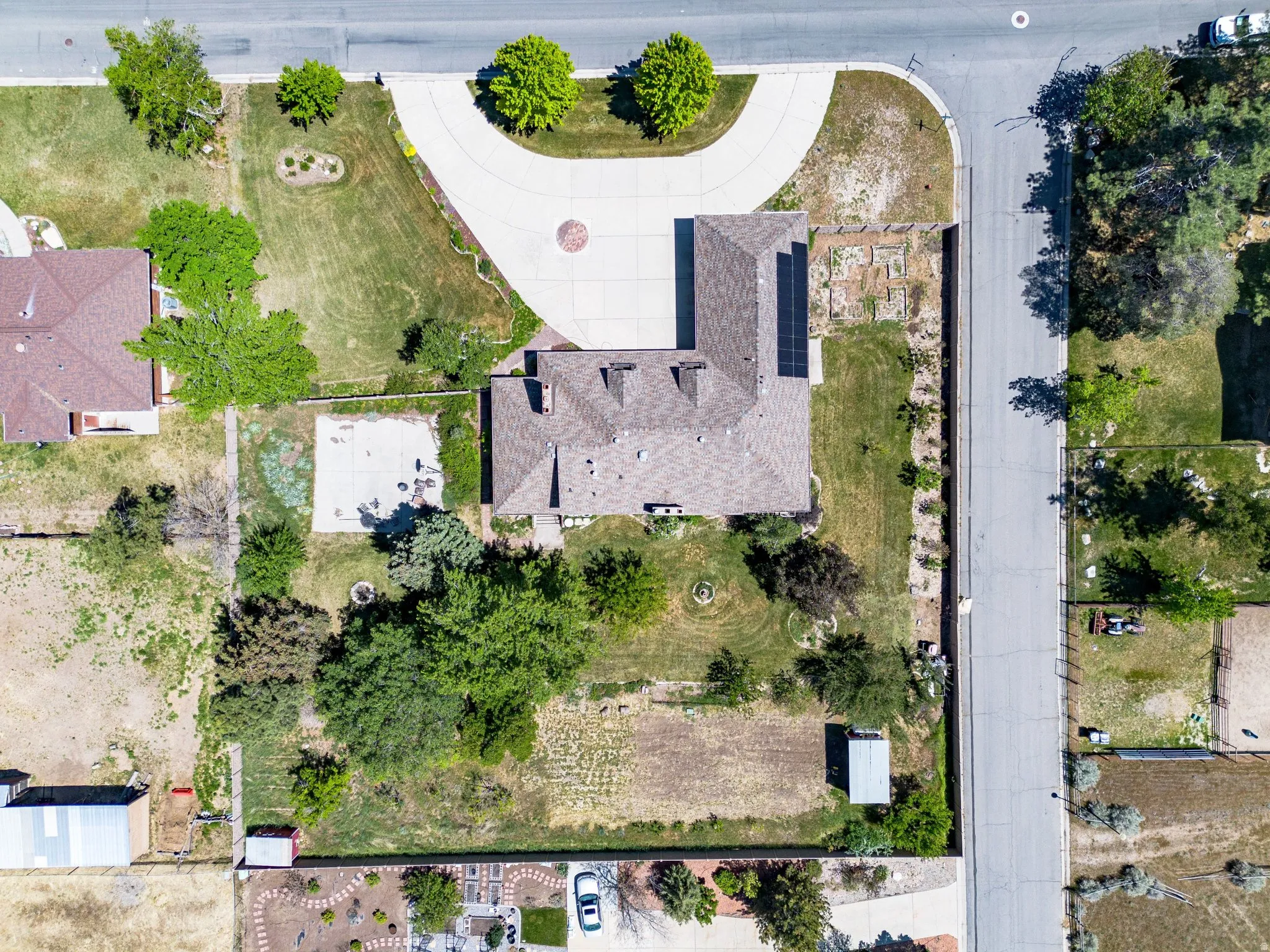 Expansive corner lot featuring a circular driveway, mature landscaping, a paved patio area, and a substantial outbuilding