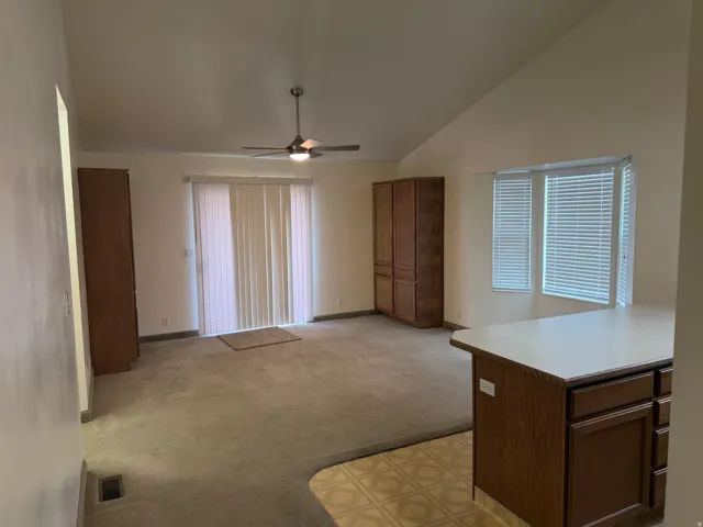 Vaulted ceiling, ceiling fan, wood-finish cabinetry, sliding glass door, and bay windows