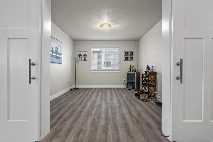 Spacious interior room featuring wood-finish flooring, a window with blinds, and light-toned walls