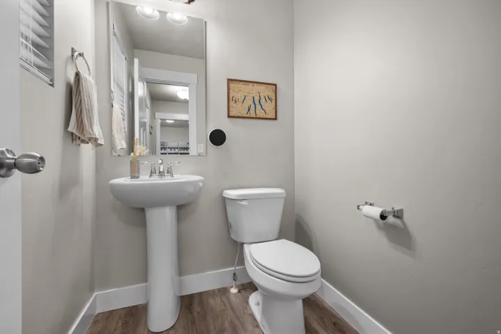 Powder room with a white pedestal sink, chrome faucet, and wood-finish flooring