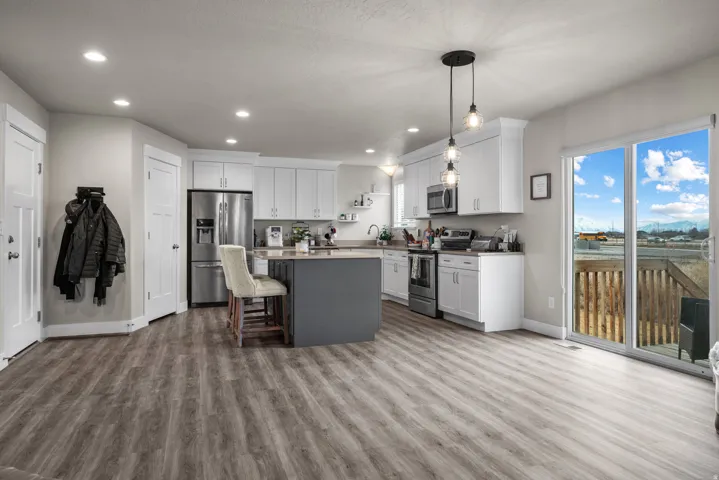 Open-concept kitchen and living area featuring wood-finish flooring, white cabinetry, a dark gray kitchen island, stainless steel appliances, and a glass sliding door leading to an outdoor deck