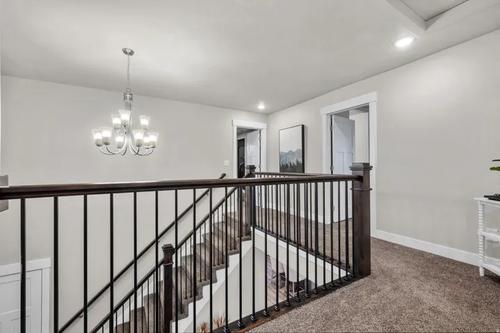 Staircase and upper landing featuring dark wood railing with black balusters, recessed lighting, and a contemporary chandelier